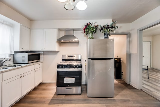 kitchen with stainless steel appliances, sink, light hardwood / wood-style flooring, wall chimney exhaust hood, and white cabinets