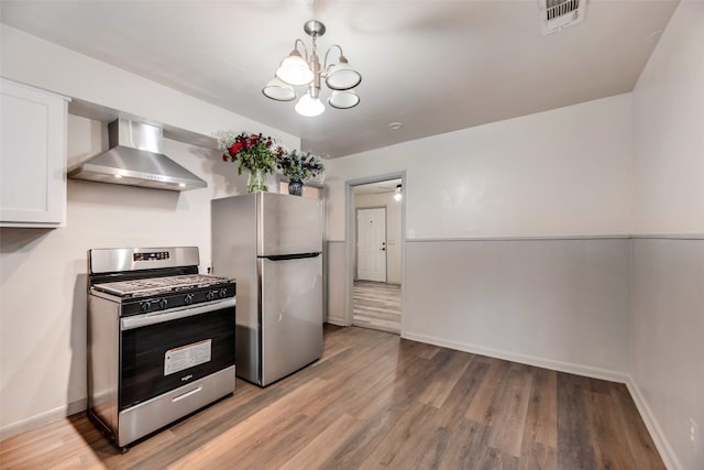 kitchen featuring an inviting chandelier, appliances with stainless steel finishes, white cabinets, light hardwood / wood-style flooring, and wall chimney range hood