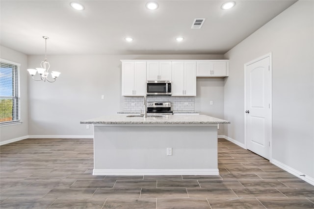 kitchen featuring a kitchen island with sink, light stone counters, stove, white cabinets, and an inviting chandelier