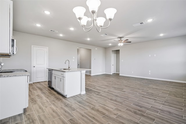 kitchen featuring pendant lighting, ceiling fan with notable chandelier, white cabinetry, a kitchen island with sink, and sink