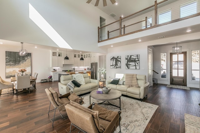 living room featuring dark hardwood / wood-style flooring, ceiling fan with notable chandelier, and a towering ceiling