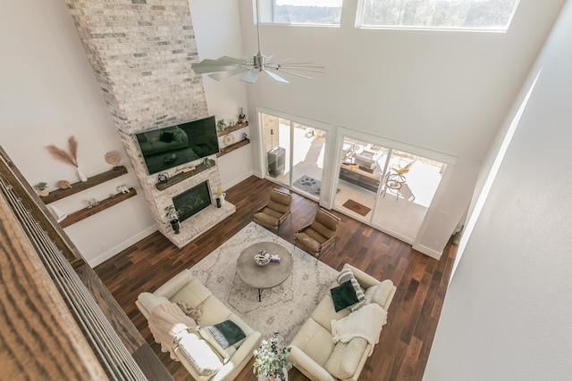 living room with ceiling fan, a stone fireplace, a towering ceiling, brick wall, and dark hardwood / wood-style floors