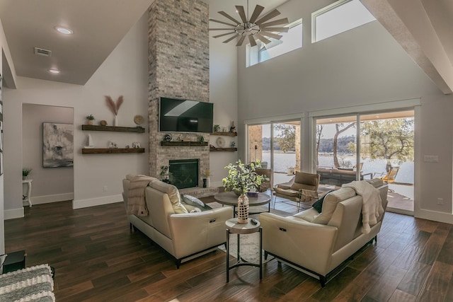 living room with plenty of natural light, high vaulted ceiling, dark wood-type flooring, and a stone fireplace