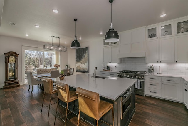 kitchen featuring white cabinets, dark hardwood / wood-style flooring, backsplash, stainless steel appliances, and a center island with sink