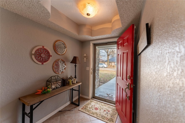 entryway with a raised ceiling, light tile floors, and a textured ceiling