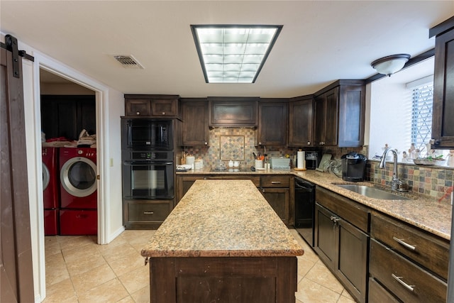 kitchen featuring black appliances, a barn door, washing machine and clothes dryer, sink, and tasteful backsplash