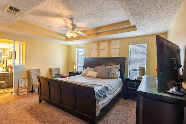 bedroom featuring a textured ceiling, ceiling fan, a tray ceiling, and multiple windows