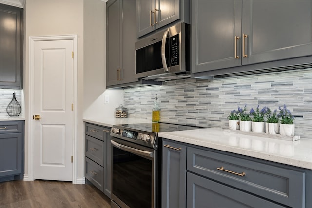 kitchen with dark wood-type flooring, appliances with stainless steel finishes, light stone counters, and tasteful backsplash