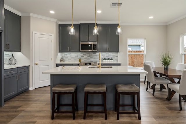 kitchen featuring dark wood-type flooring, backsplash, an island with sink, sink, and gray cabinetry