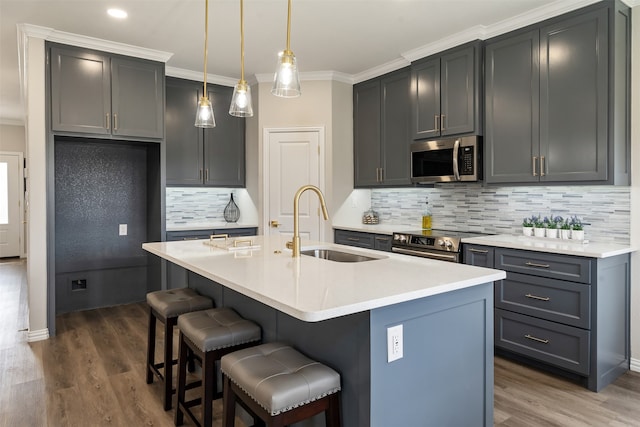 kitchen featuring stainless steel appliances, hardwood / wood-style floors, decorative backsplash, crown molding, and a kitchen island with sink