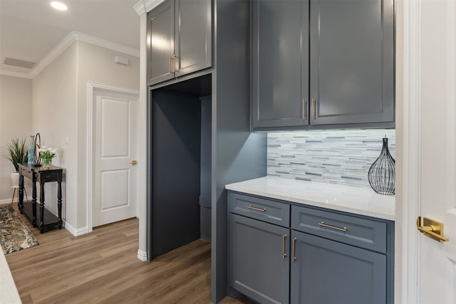 kitchen with gray cabinetry, light stone counters, decorative backsplash, wood-type flooring, and ornamental molding