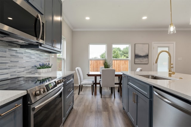 kitchen featuring tasteful backsplash, light stone countertops, appliances with stainless steel finishes, wood-type flooring, and sink