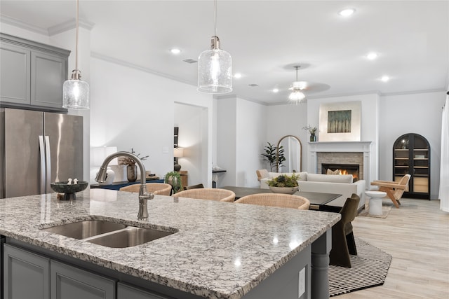 kitchen with gray cabinetry, stainless steel refrigerator, pendant lighting, light hardwood / wood-style flooring, and sink