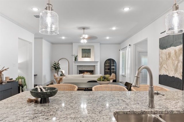 kitchen featuring ceiling fan, hanging light fixtures, sink, light stone countertops, and crown molding