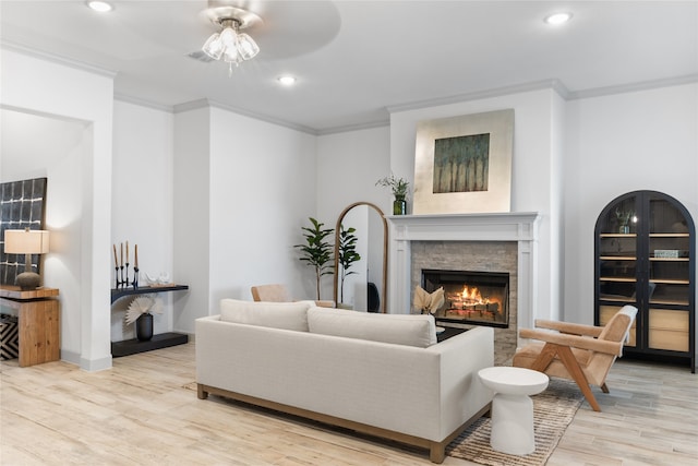 living room with light hardwood / wood-style floors, a stone fireplace, ornamental molding, and ceiling fan