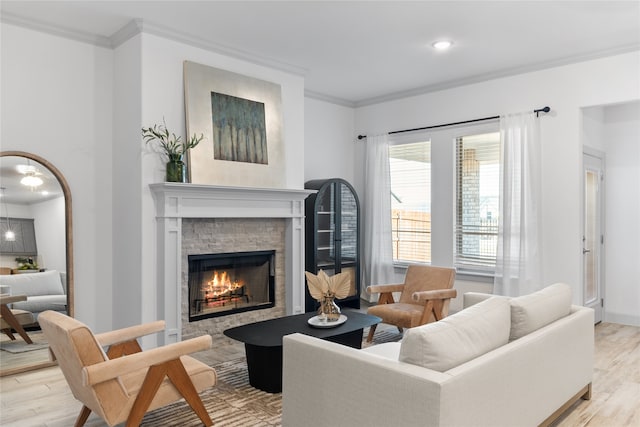 living room featuring light hardwood / wood-style floors, crown molding, and a stone fireplace