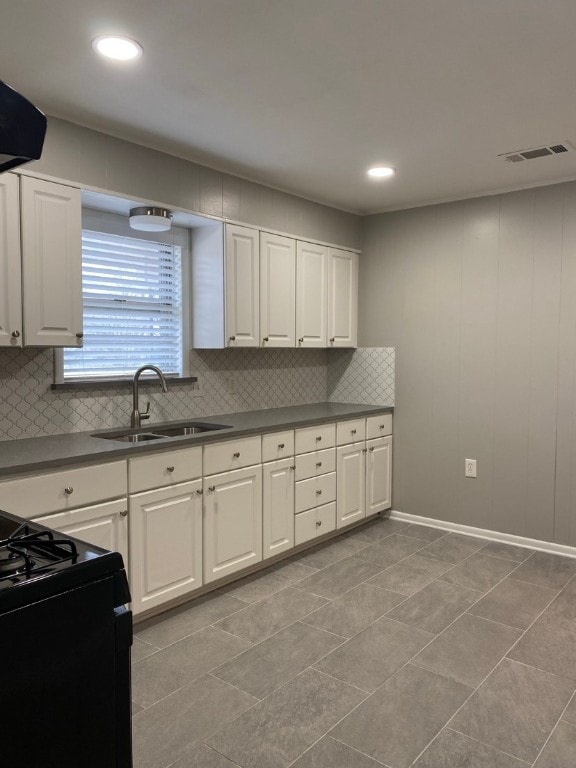 kitchen with tasteful backsplash, black electric range oven, white cabinets, light tile floors, and sink