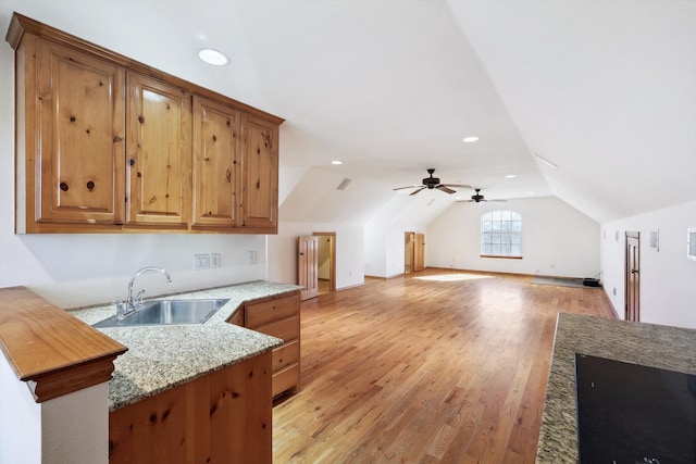 kitchen featuring light stone countertops, light hardwood / wood-style floors, sink, lofted ceiling, and ceiling fan