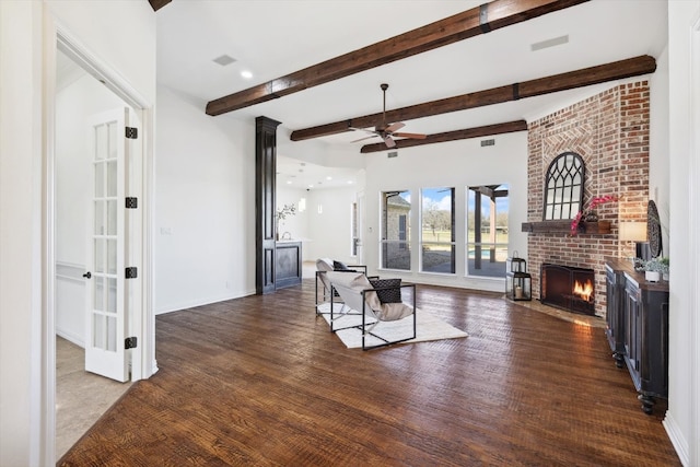 living room featuring ceiling fan, dark hardwood / wood-style floors, beamed ceiling, and a fireplace