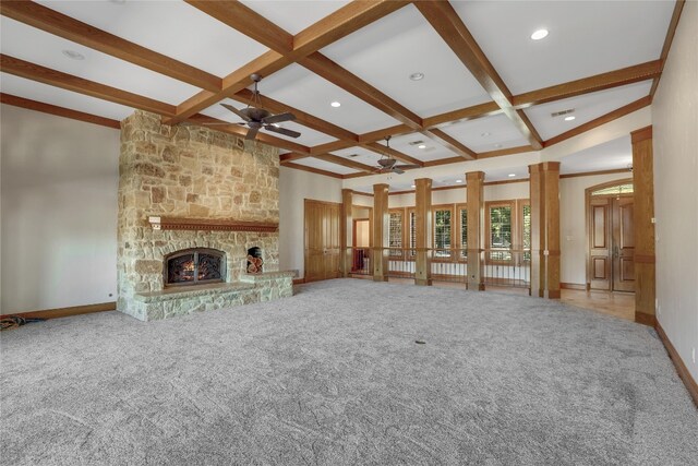 unfurnished living room featuring beam ceiling, coffered ceiling, carpet floors, and a stone fireplace