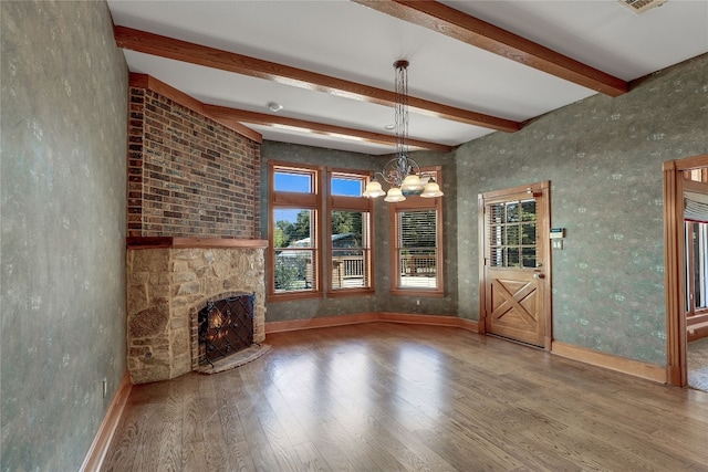 unfurnished living room with beam ceiling, an inviting chandelier, a stone fireplace, and dark wood-type flooring