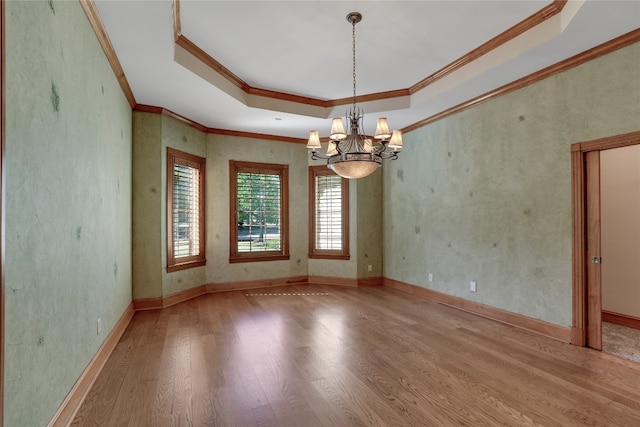 unfurnished room featuring a raised ceiling, ornamental molding, a notable chandelier, and light wood-type flooring