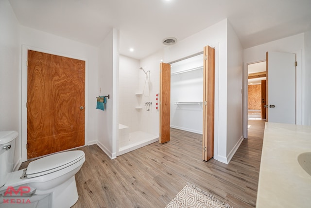 bathroom featuring hardwood / wood-style flooring, vanity, a tile shower, and toilet