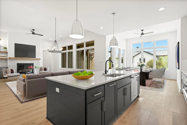 kitchen with ceiling fan with notable chandelier, sink, an island with sink, light hardwood / wood-style floors, and hanging light fixtures