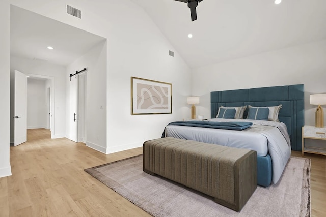 bedroom with a barn door, ceiling fan, high vaulted ceiling, and light wood-type flooring