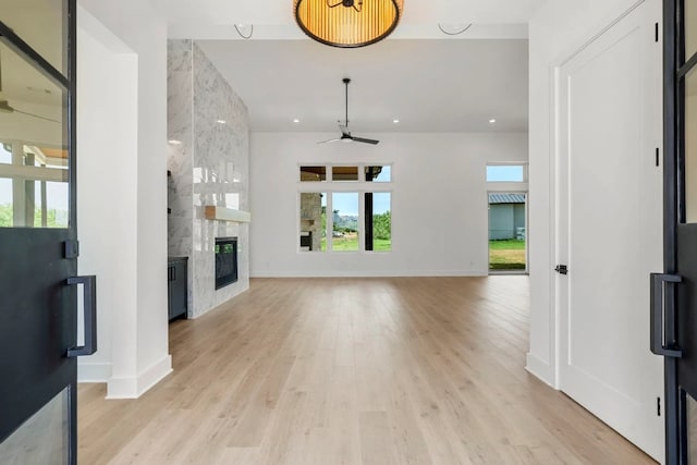 unfurnished living room featuring a large fireplace, ceiling fan, and light wood-type flooring