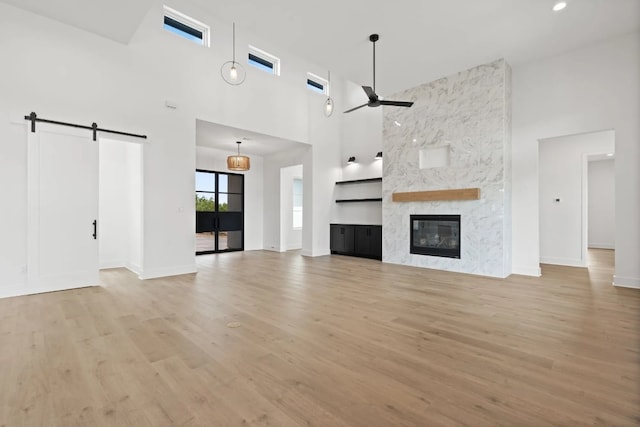 unfurnished living room featuring a fireplace, a barn door, ceiling fan, light hardwood / wood-style flooring, and a towering ceiling