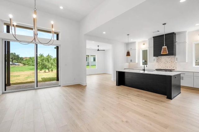 kitchen with tasteful backsplash, a center island with sink, decorative light fixtures, and light wood-type flooring