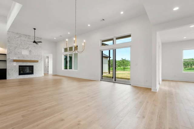 unfurnished living room featuring a fireplace, ceiling fan with notable chandelier, and light wood-type flooring