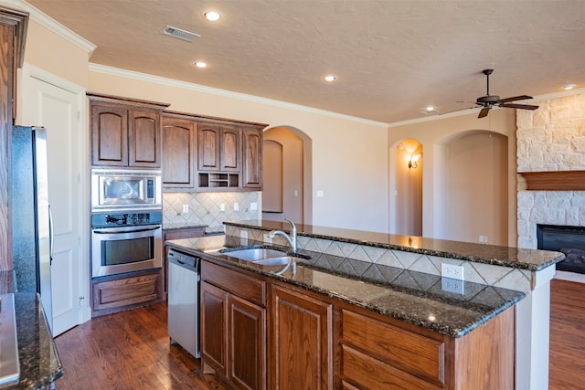 kitchen featuring dark hardwood / wood-style floors, an island with sink, ceiling fan, stainless steel appliances, and a fireplace