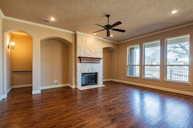 unfurnished living room featuring ceiling fan, dark wood-type flooring, a textured ceiling, a stone fireplace, and ornamental molding