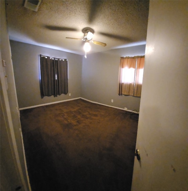 empty room featuring a textured ceiling, ceiling fan, and dark colored carpet