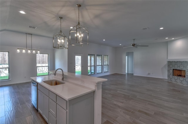 kitchen featuring an island with sink, a fireplace, ceiling fan with notable chandelier, white cabinetry, and sink