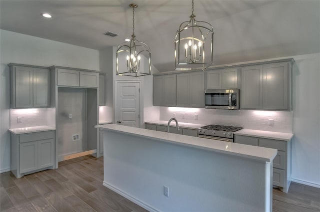 kitchen featuring backsplash, hanging light fixtures, stainless steel appliances, and an island with sink