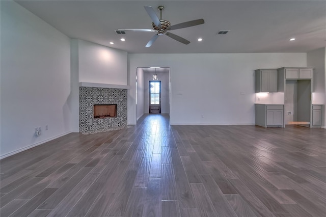 unfurnished living room featuring a tile fireplace, dark wood-type flooring, and ceiling fan