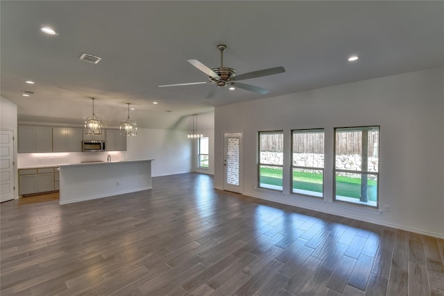 unfurnished living room with a healthy amount of sunlight, dark wood-type flooring, and ceiling fan with notable chandelier