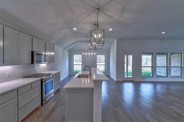 kitchen featuring an island with sink, sink, dark hardwood / wood-style flooring, appliances with stainless steel finishes, and a notable chandelier