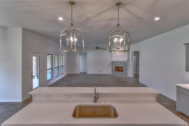 kitchen featuring dark hardwood / wood-style floors, ceiling fan with notable chandelier, sink, and a fireplace