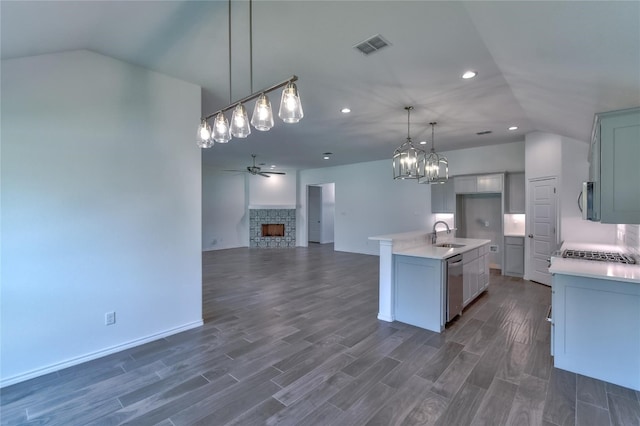 kitchen with lofted ceiling, ceiling fan with notable chandelier, a center island with sink, a stone fireplace, and dark hardwood / wood-style flooring