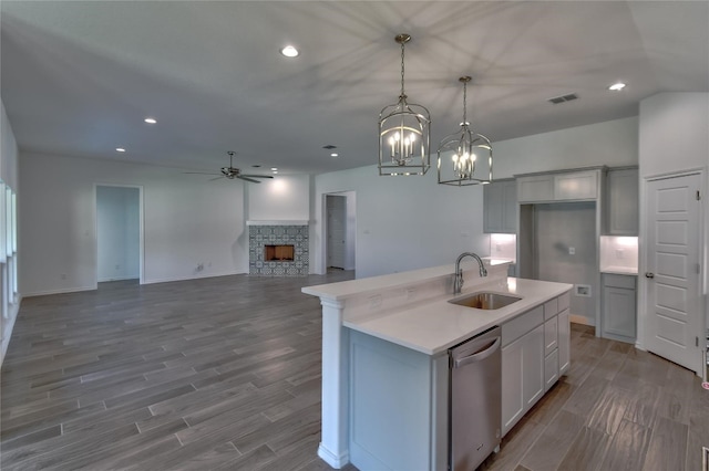 kitchen with an island with sink, pendant lighting, stainless steel dishwasher, ceiling fan with notable chandelier, and a stone fireplace