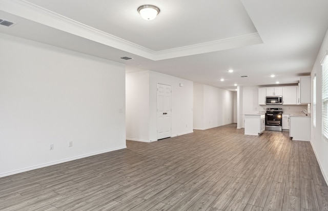 unfurnished living room featuring light hardwood / wood-style floors, sink, crown molding, and a tray ceiling