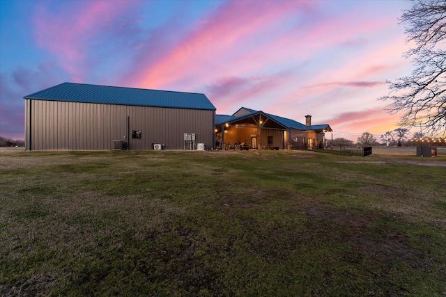 back of house featuring an outbuilding, metal roof, central AC, an outdoor structure, and a yard