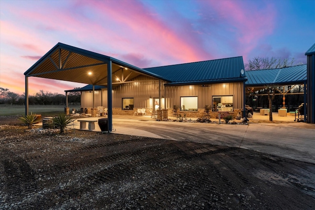 front of property at dusk with metal roof, an attached carport, board and batten siding, and a patio area