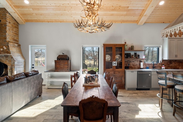 dining space with a stone fireplace, light hardwood / wood-style flooring, wooden ceiling, and beamed ceiling