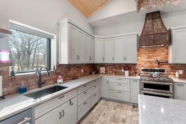 kitchen with lofted ceiling, sink, appliances with stainless steel finishes, premium range hood, and backsplash