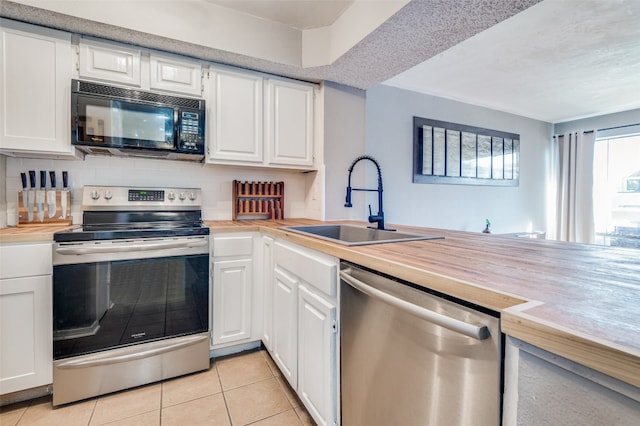 kitchen featuring appliances with stainless steel finishes, light tile floors, sink, kitchen peninsula, and white cabinetry